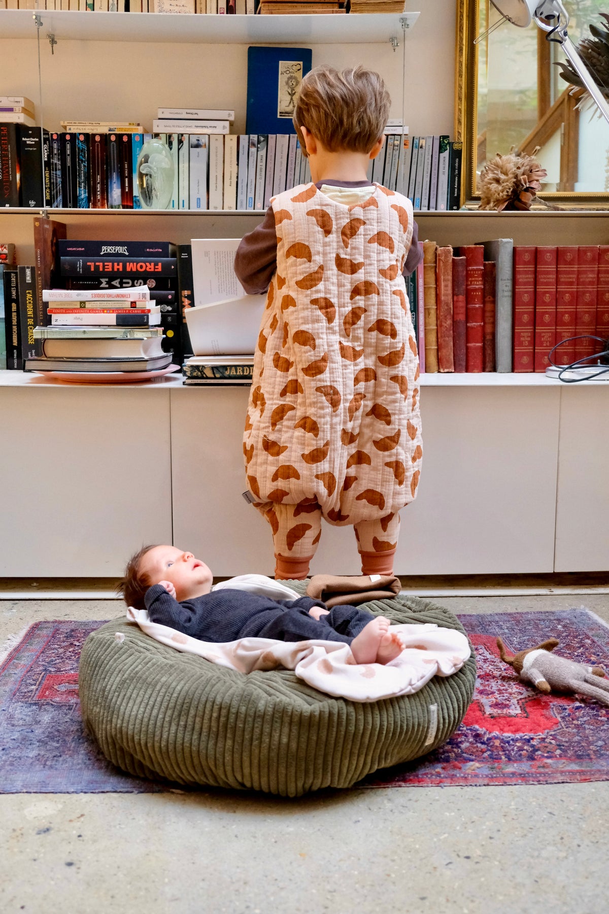enfant de dos avec gigoteuse à pied avec devant lui un bébé sur un nid matcha